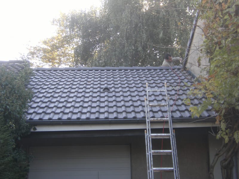 Couvreur au travail sur une toiture de garage en tuiles grises